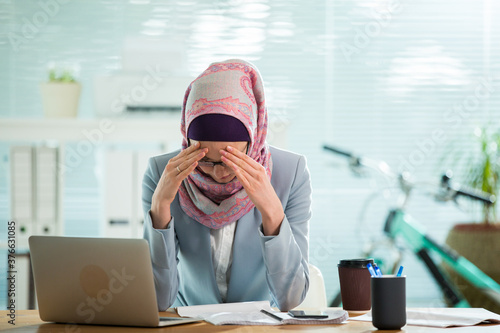 Wallpaper Mural Beautiful young working woman in hijab, suit and eyeglasses sitting in office, having headache. Modern light office with big window.  Torontodigital.ca