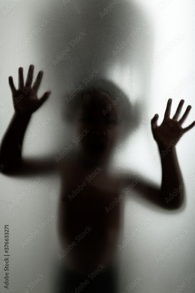 Ghost concept shadow of a child behind the matte glass blurry hand and body soft focus