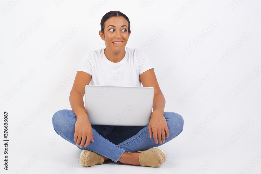 Dreamy young female with thoughtful expression, looks away keeps hands down bitting her lip thinks about something pleasant poses against gray wall. Dreamy young female with thoughtful expression, looks away keeps hands down bitting her lip thinks about something pleasant poses against gray wall.