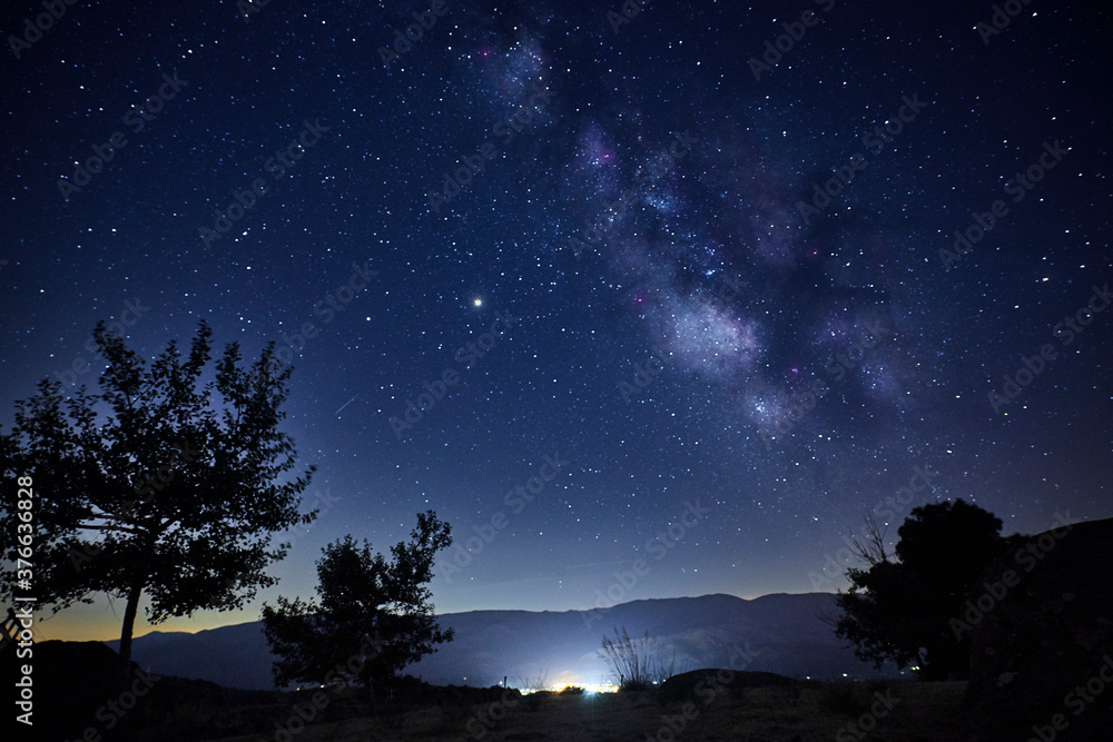 View of the Milky Way over the lights of a mountain village View of the Milky Way over the lights of a mountain village