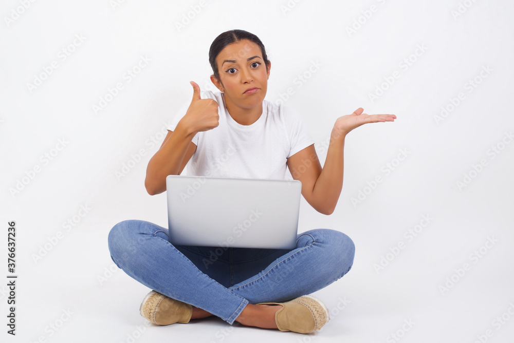 Young happy cheerful woman showing thumb up and pointing with the other hand while standing outdoors. Good Job. Wearing casual clothes. Young happy cheerful woman showing thumb up and pointing with the other hand while standing outdoors. Good Job. Wearing casual clothes.