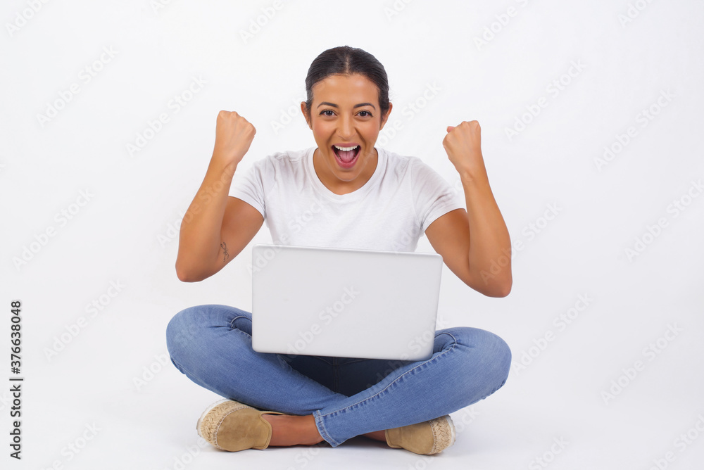 Waist up portrait of strong successful determined young female winner in casual t-shirt raising arms, clenching fists, exclaiming with joy and excitement. Victory, success and achievement concept. Waist up portrait of strong successful determined young female winner in casual t-shirt raising arms, clenching fists, exclaiming with joy and excitement. Victory, success and achievement concept.