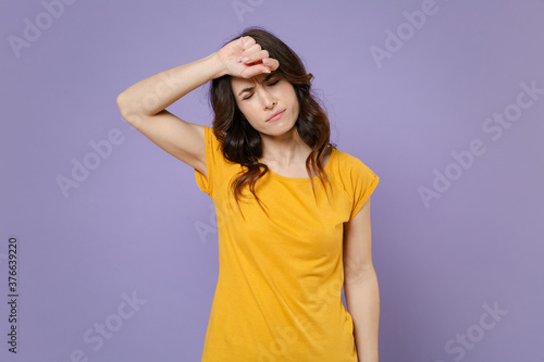 Tired exhausted dissatisfied young brunette woman 20s wearing basic yellow t-shirt posing standing put hand on head keeping eyes closed isolated on pastel violet colour background, studio portrait.