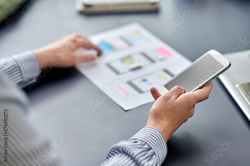 business, people and technology concept - close up of ui designer with smartphone and mockups working on mobile app design at office