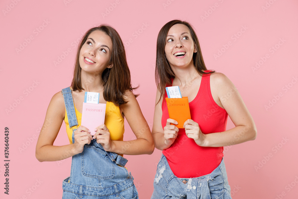 Two funny pensive young brunette traveler tourist women friends 20s in casual denim clothes hold passport ticket boarding pass looking up isolated on pastel pink colour background studio portrait. Two funny pensive young brunette traveler tourist women friends 20s in casual denim clothes hold passport ticket boarding pass looking up isolated on pastel pink colour background studio portrait.