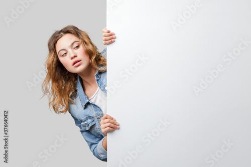 Young woman peeking out from behind a white wall photo