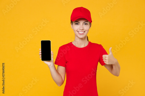 Delivery employee woman in red cap blank t-shirt uniform work courier in service during quarantine coronavirus covid-19 virus hold mobile phone black screen mockup isolated on yellow background studio © ViDi Studio