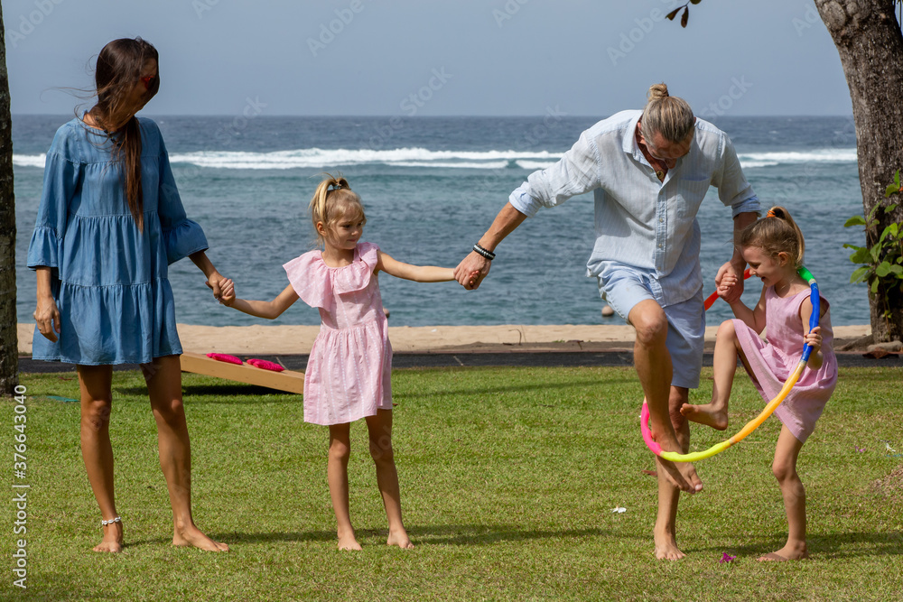 Parents playing exciting hula hoop pass game with children by the sea during summer vacation. Family spending quality time together Parents playing exciting hula hoop pass game with children by the sea during summer vacation. Family spending quality time together