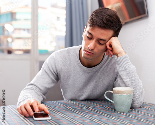 Young man is sad sitting with phone because she is alone at home photo