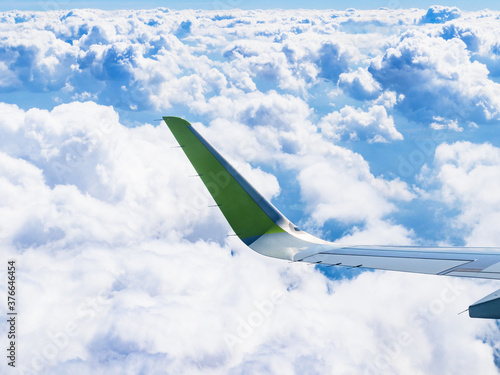 airplane wing over white cumulus clouds in blue sky during flight on summer day