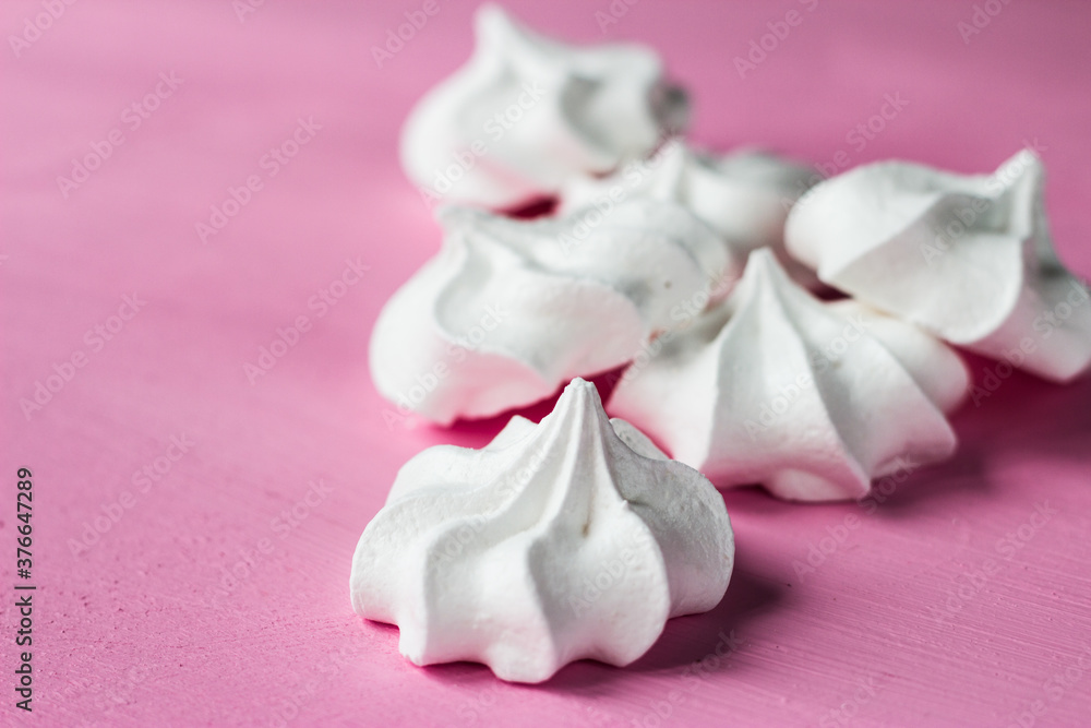 White marshmallows on a pink background. Meringues lie on a bright table
