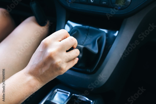 Woman is holding manual gearbox in the car. Girl is driving.