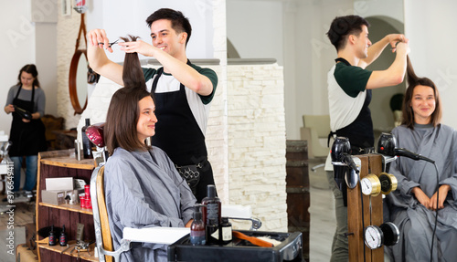 Young man professional hairdresser cut female's hair in hairdressing salon