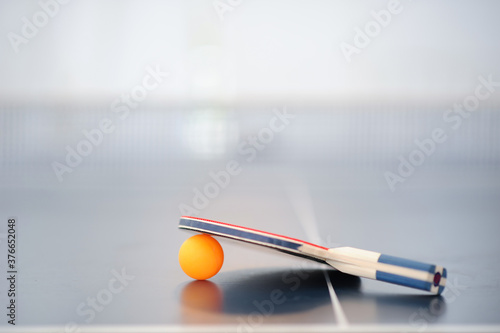 Selective focus Table tennis racket is placed over the orange ping pong ball on the table tennis table..