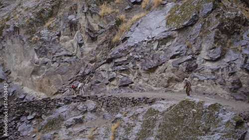 an Afghan with a donkey loaded with luggage are walking along a mountain road along the border photo