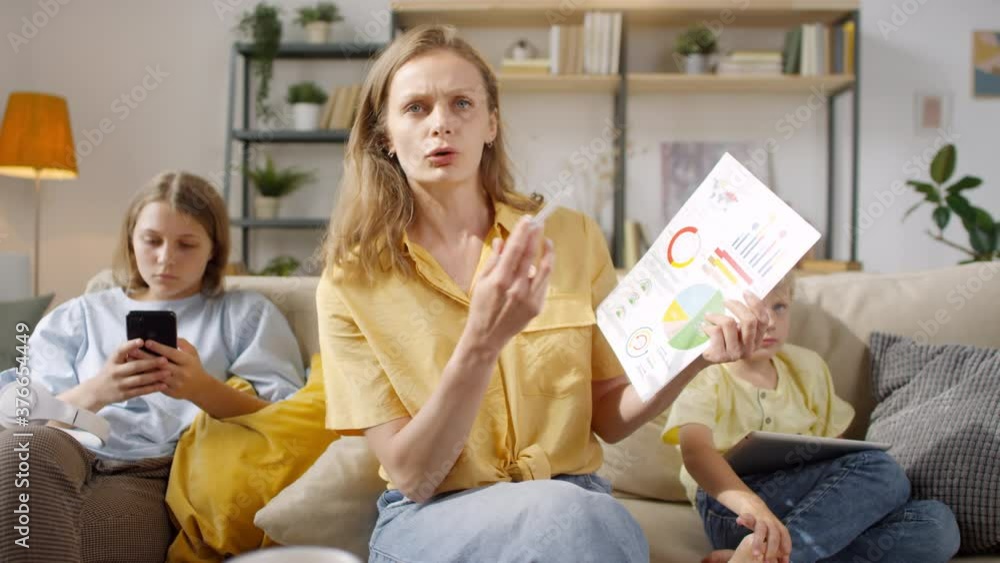 POV of woman with financial document sitting on couch and talking on video call with colleagues while her teenage daughter with mobile phone and little boy with tablet sitting beside her POV of woman with financial document sitting on couch and talking on video call with colleagues while her teenage daughter with mobile phone and little boy with tablet sitting beside her