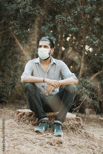 Selective focus shot of an attractive male sitting on the ground and wearing a facial mask
