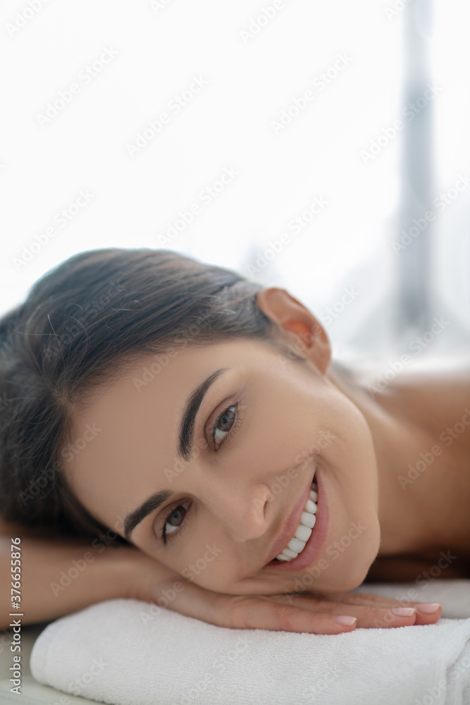 Dark-haired woman lying down after beauty procedures and smiling