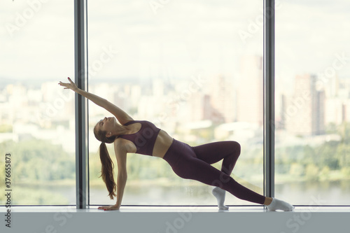 Fototapeta Naklejka Na Ścianę i Meble -  Young beautiful woman training with a view of the city in the background. The concept of health and motivation, stretching and training in the gym.