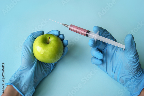 Green apple and syringe with GMO in hands on a blue background.