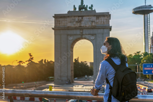 Young Hispanic male with a medical mask enjoying the beautiful view of a monument in Moncloa, Spain photo