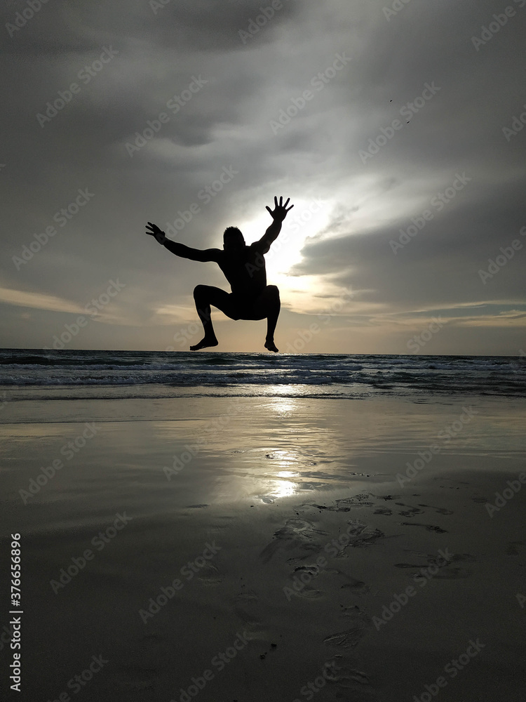 Fototapeta premium Sunset in the beach with a men silhouette jumping with the arms open