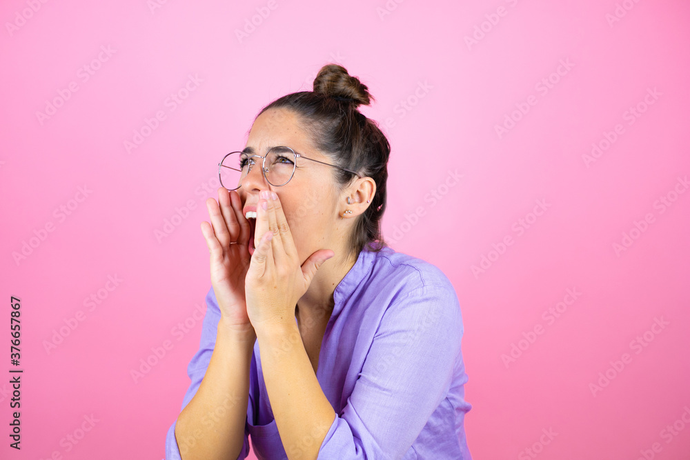 Young beautiful woman wearing glasses over isolated pink background shouting and screaming loud to side with hands on mouth Young beautiful woman wearing glasses over isolated pink background shouting and screaming loud to side with hands on mouth