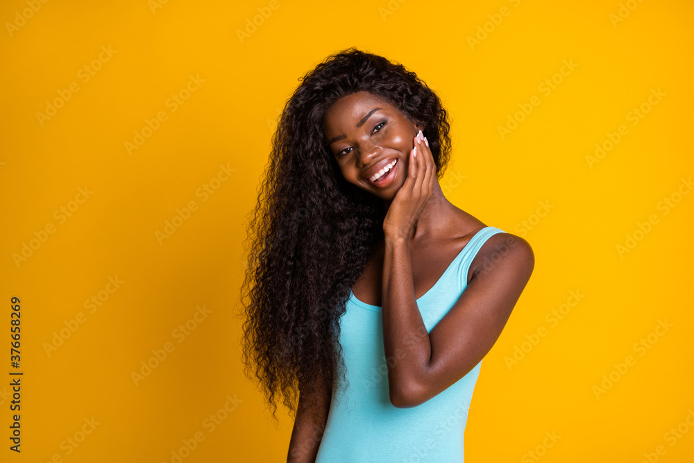 Photo portrait of charming african american girl with perfect skin touching face with hand smiling isolated on vivid yellow colored background Photo portrait of charming african american girl with perfect skin touching face with hand smiling isolated on vivid yellow colored background
