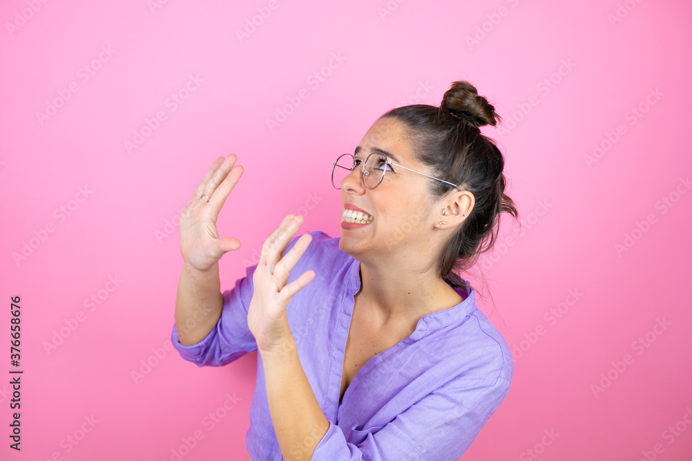 Young beautiful woman wearing glasses over isolated pink background scared with her arms up like something falling from above Young beautiful woman wearing glasses over isolated pink background scared with her arms up like something falling from above