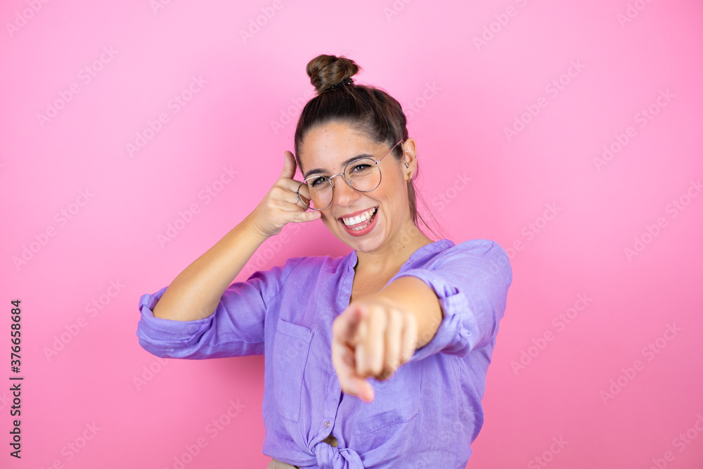 Young beautiful woman wearing glasses over isolated pink background doing the “call me” gesture with her hands.