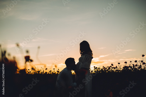 Silhouette of happy couple at sunset, the husband kisses the pregnant wife in the belly against the background of a romantic sunset. Copy space.