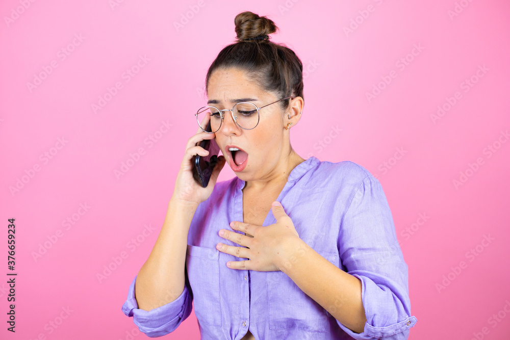 Young beautiful woman wearing glasses over isolated pink background talking on the phone with a worried expression Young beautiful woman wearing glasses over isolated pink background talking on the phone with a worried expression