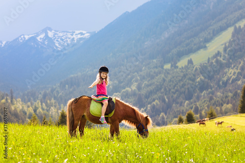 Kids riding pony. Child on horse in Alps mountains © famveldman
