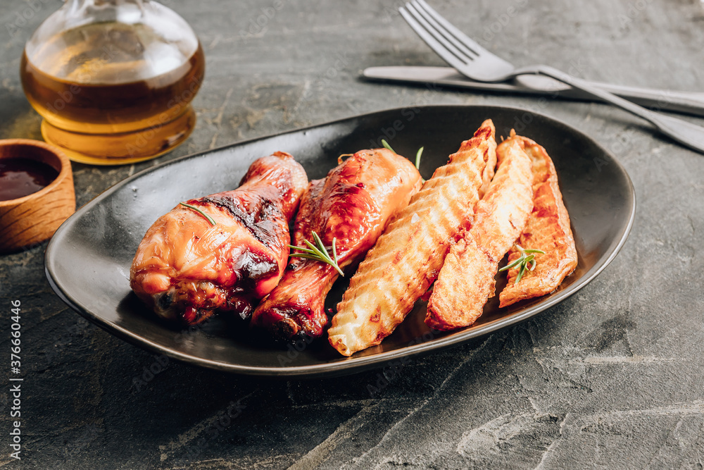 Chicken drumsticks with french fries on black plate on rustic black background. Chicken drumsticks with french fries on black plate on rustic black background.