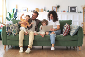 Young beautiful happy family relaxing on the sofa and  look at the laptop at home. 