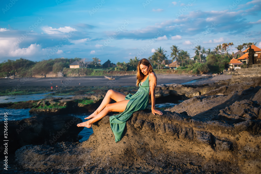 Stylish woman sitting on rocky shore on Bali