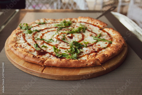 Pizza with arugula on a wooden plate on grey background in summer terrace
