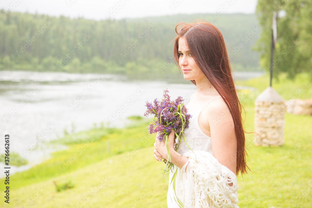 Fototapeta premium Girl with wildflowers on field in cloudy day