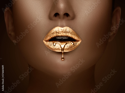 Golden lipstick closeup. Liquid metal dripping from gold lips. Beautiful makeup. Sexy lips, bright liquid paint on beauty model girl's mouth, close-up. Lipstick. © Subbotina Anna