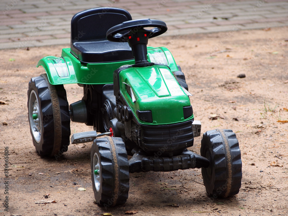 A children's toy tractor with a pedal drive stands on the Playground. Educational toys for children, outdoor activities.