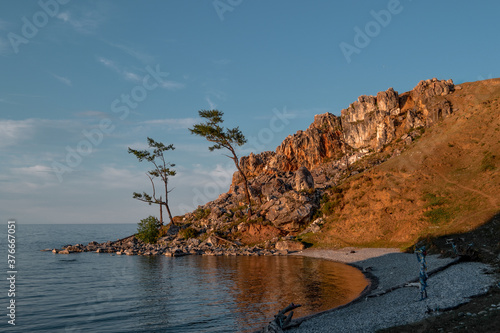 Red stones rock in the light of the setting sun, by the bay with the coast on lake Baikal, reflection, coniferous larch trees