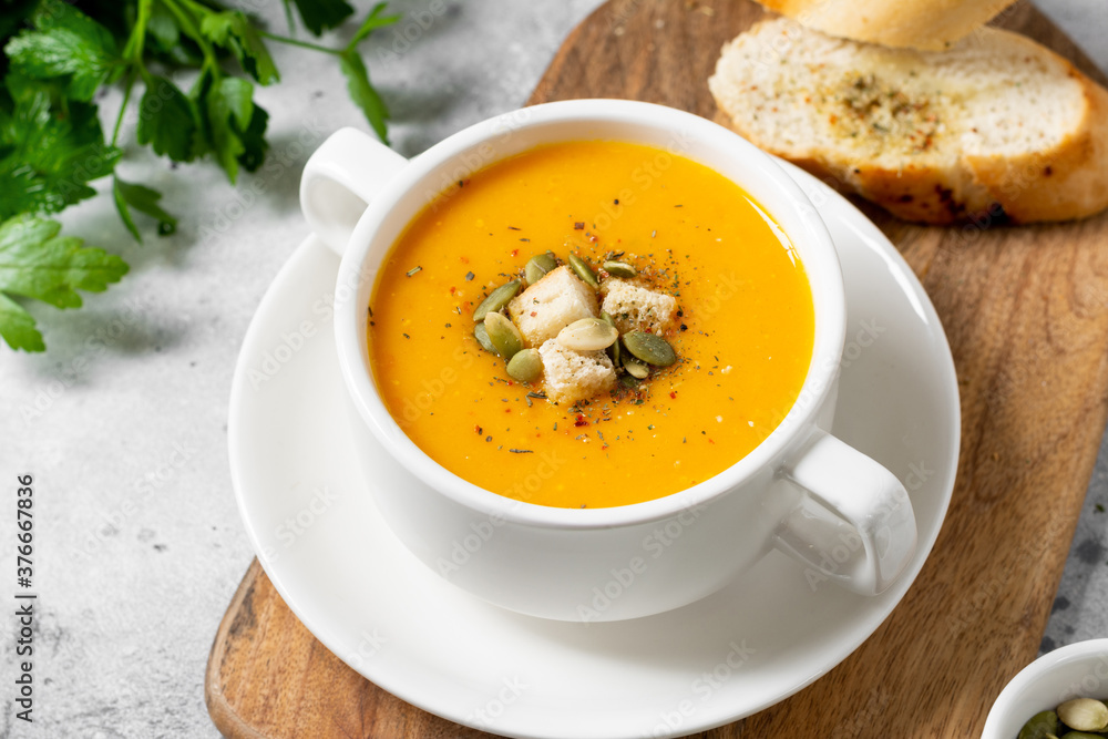 Pumpkin soup. Pumpkin cream soup in a white plate on the light gray kitchen table. Vegetarian autumn soup close up Pumpkin soup. Pumpkin cream soup in a white plate on the light gray kitchen table. Vegetarian autumn soup close up
