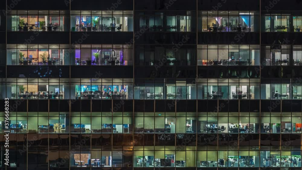 Modern office building with big windows at night timelapse close up view, in windows glowing light shines and some people inside, Singapore. Pan right Modern office building with big windows at night timelapse close up view, in windows glowing light shines and some people inside, Singapore. Pan right