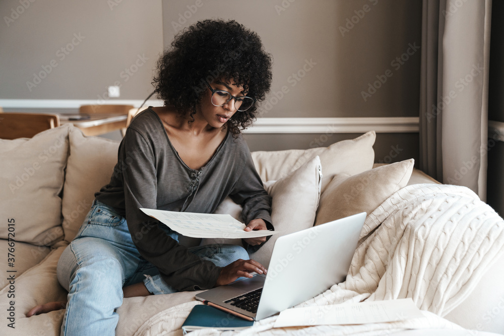 Image of thinking african american woman working with laptop and papers Image of thinking african american woman working with laptop and papers
