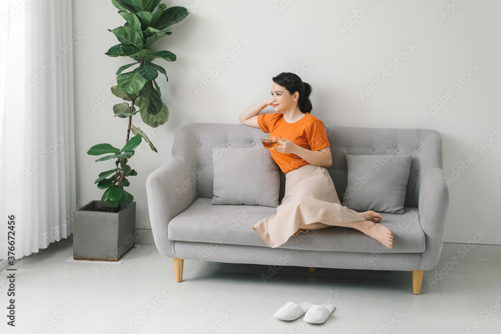Obraz premium Attractive young woman drinking a cup of tea while relaxing on a sofa at home