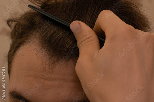 a young man tries to comb his coarse dark brown hair with a comb