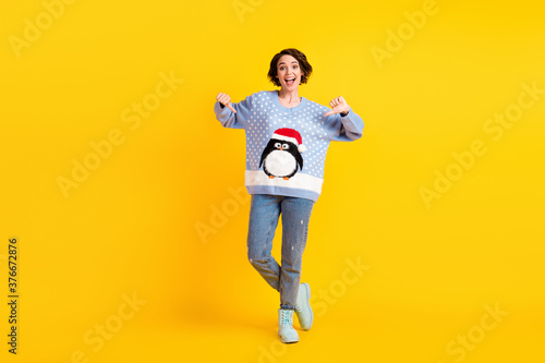 Full size photo of pretty charming lady x-mas party direct fingers showing friends new jumper funky cute fluffy penguin wear ugly ornament sweater jeans boots isolated yellow color background