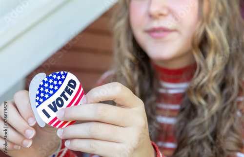 Young First time voter female peeling I voted sticker, focus on sticker