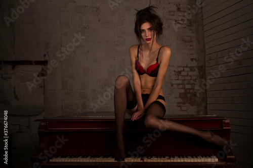 sexy leggy girl in black stockings sits on a piano in a dark room