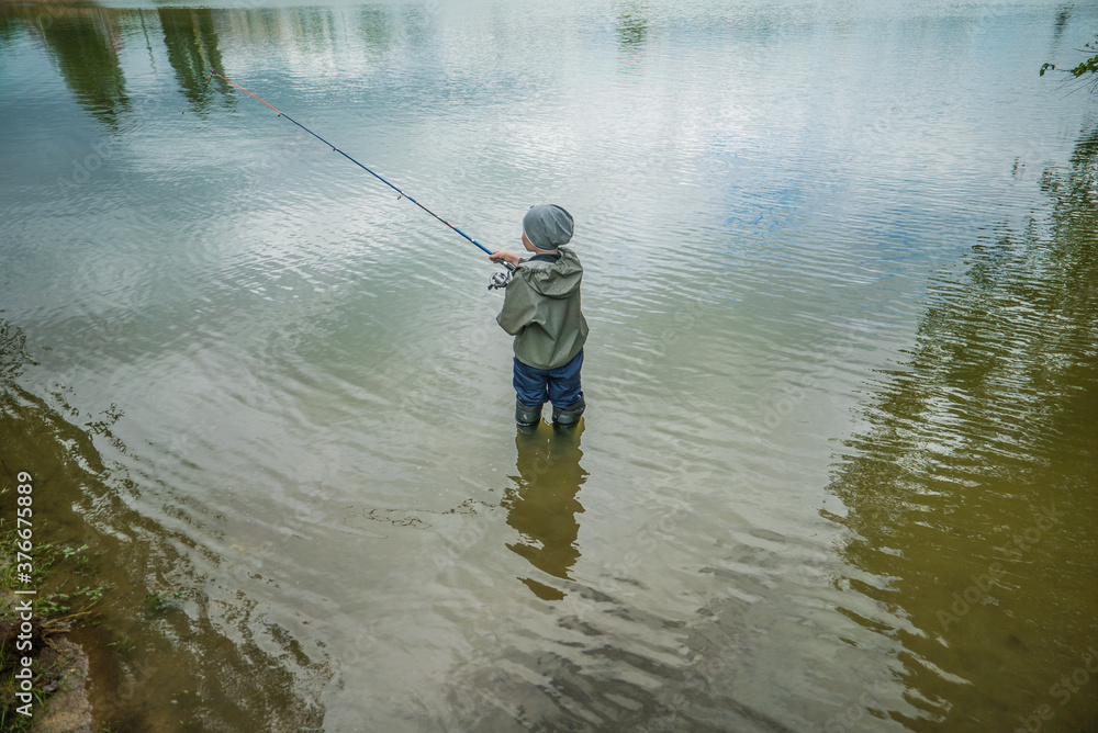 boy catching fish standing in water in big boots boy catching fish standing in water in big boots